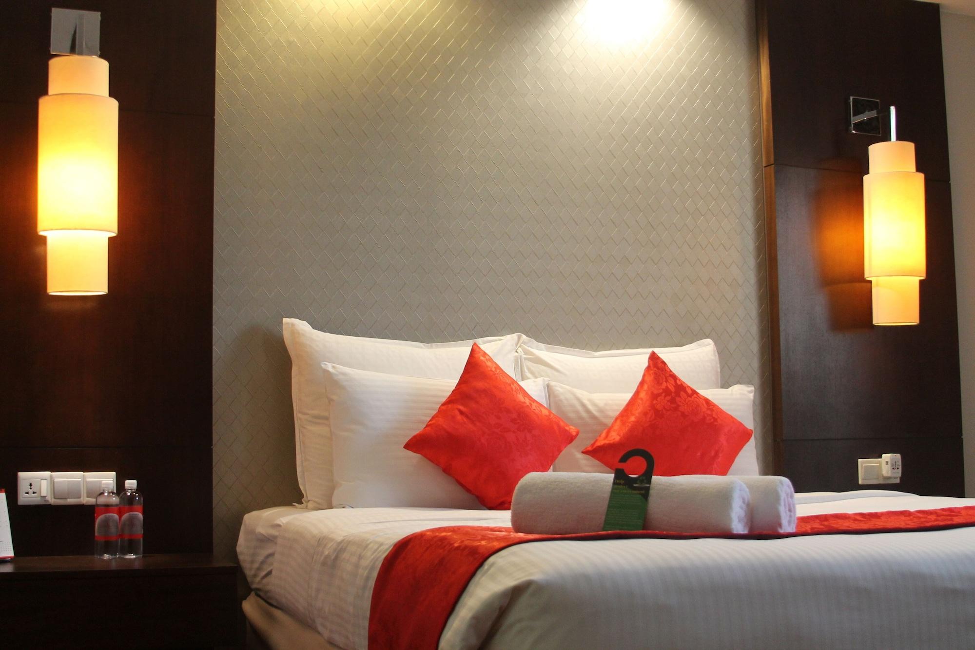 吉隆坡斯里太平洋酒店 外观 照片 The photo shows a cozy hotel room with a neatly made bed featuring white linens and decorative red accent pillows. The headboard is dark wood, and on either side of the bed, there are softly glowing wall lamps. At the foot of the bed, there are rolle