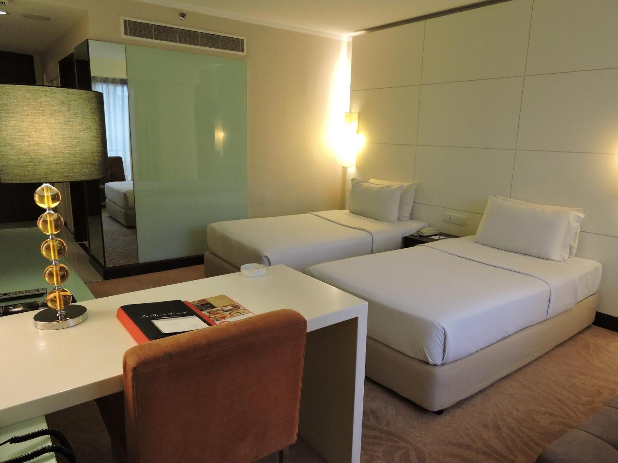 吉隆坡斯里太平洋酒店 客房 照片 The photo shows a modern hotel room featuring two single beds with white bedding. There is a minimalist design with a light-colored scheme. A small desk with a brown chair is positioned nearby, along with a lamp that has a decorative base. The room h