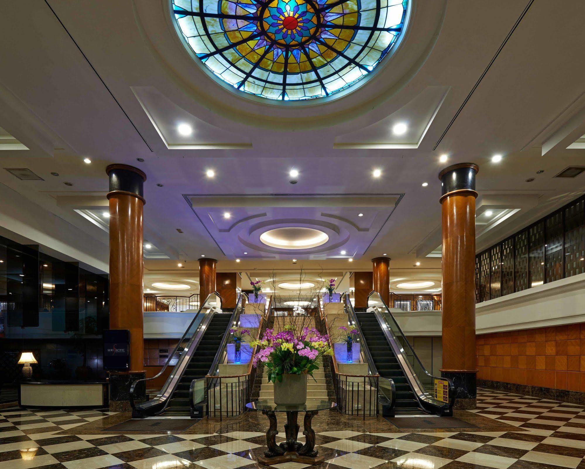 吉隆坡斯里太平洋酒店 外观 照片 The photo depicts an elegant hotel lobby featuring a large stained glass ceiling that adds a colorful touch to the space. The lobby has polished marble flooring with a checkerboard pattern. In the center, there is a beautiful arrangement of flowers i